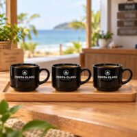 Três xícaras pretas personalizadas com o logotipo de uma pousada, na bandeja da recepção